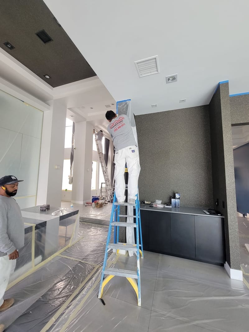 Interior painting in progress with painters on ladder applying dark accent wall