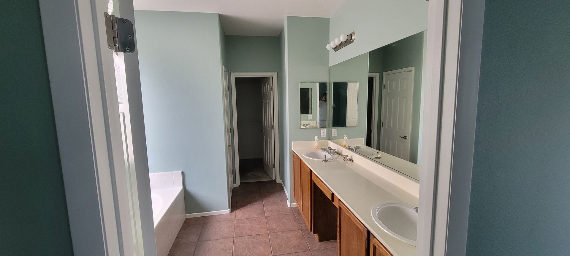 Bathroom with a long vanity, mirrors, and a tub, painted blue-green walls.