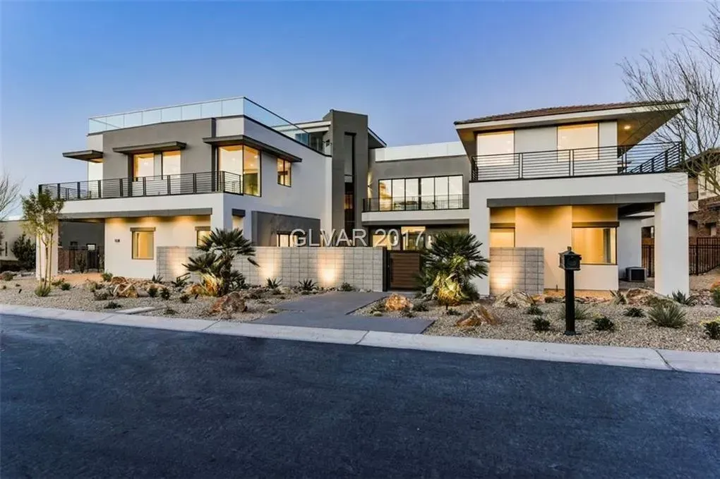 Modern, two-story house with gray and white exterior, balconies, and landscaped front yard.
