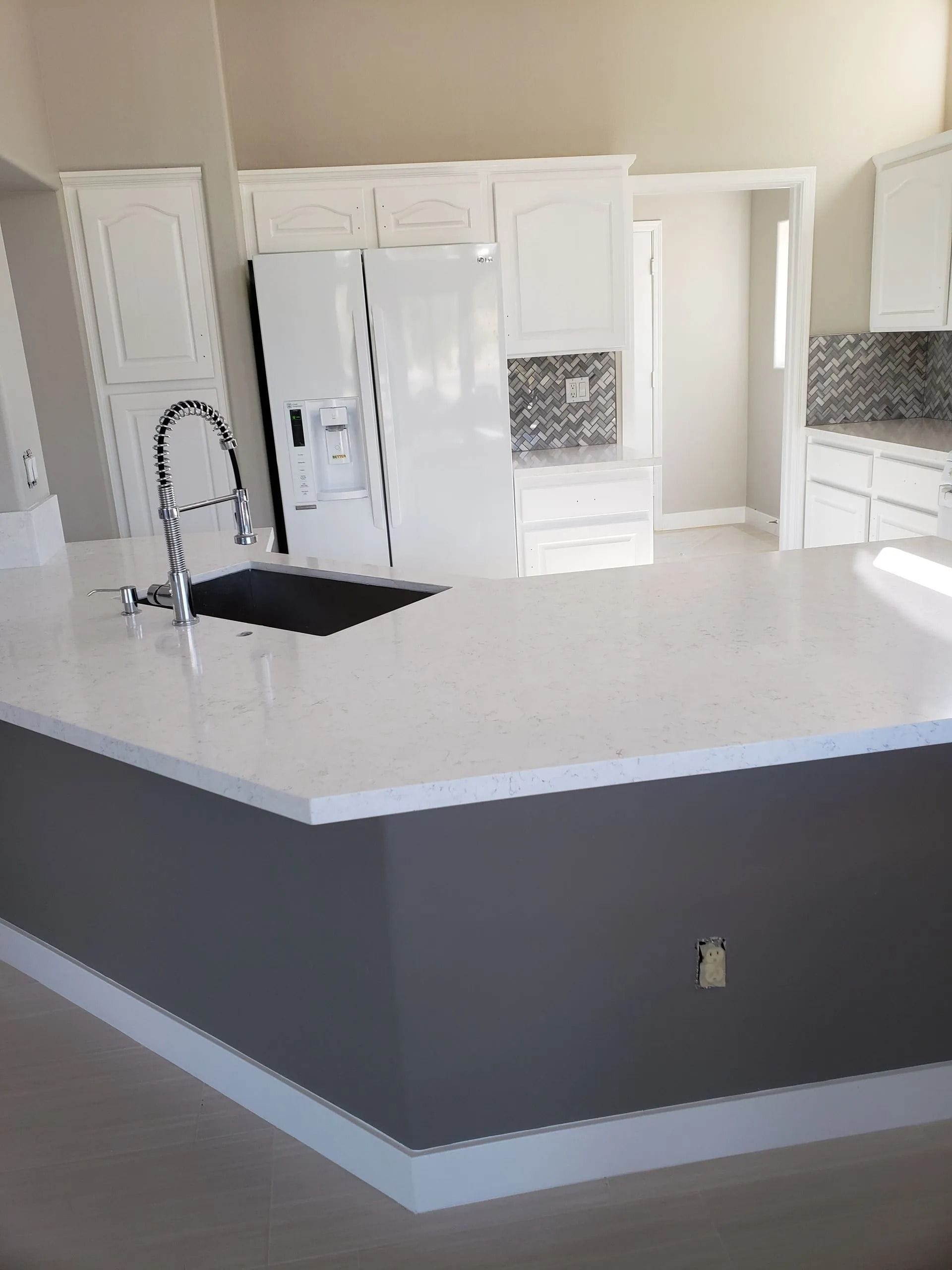 Modern kitchen with white countertops and cabinets, gray island, and stainless steel faucet.