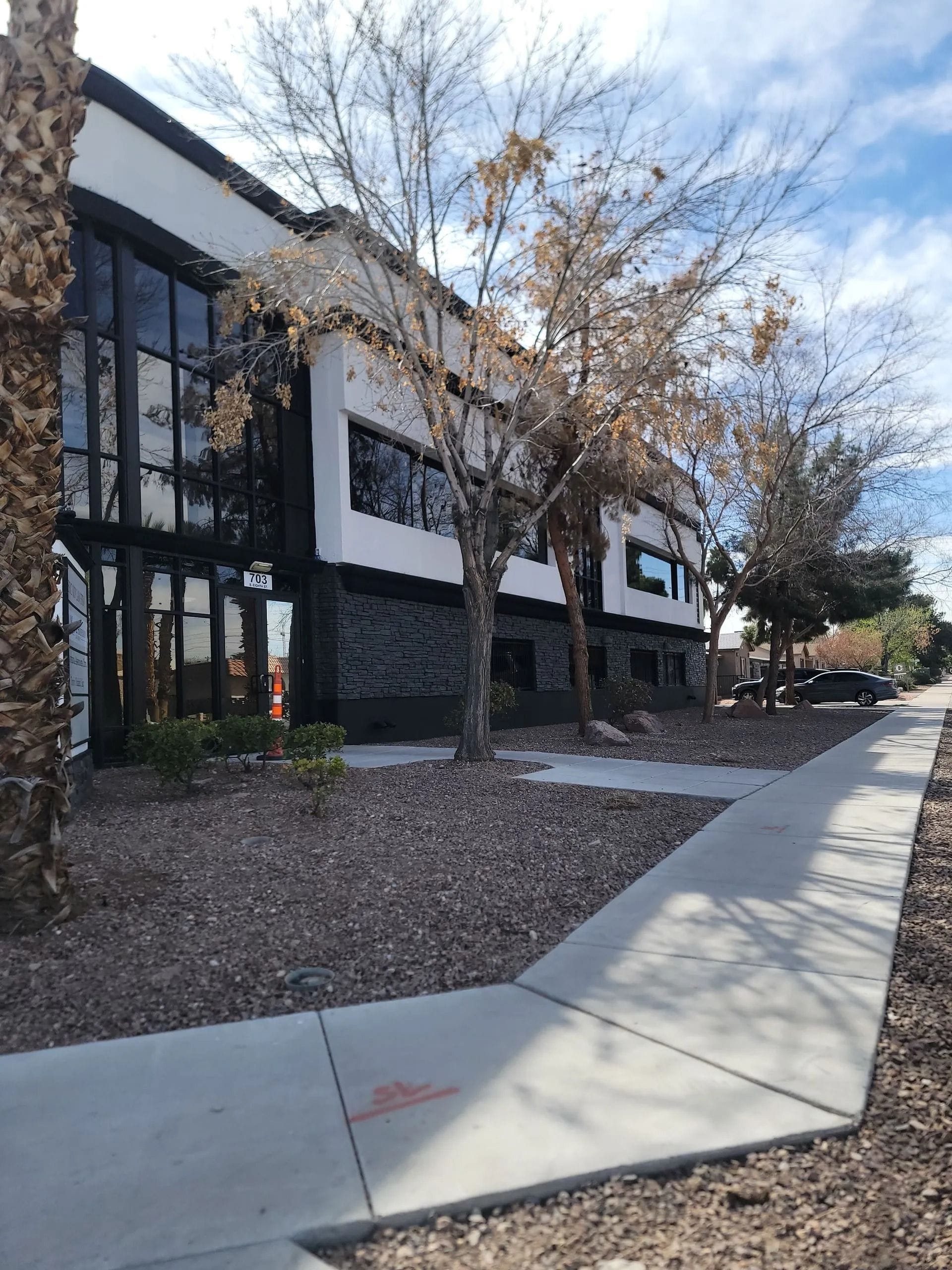 Modern building with black trim, large windows, and a stone facade. Sidewalk and trees in front.
